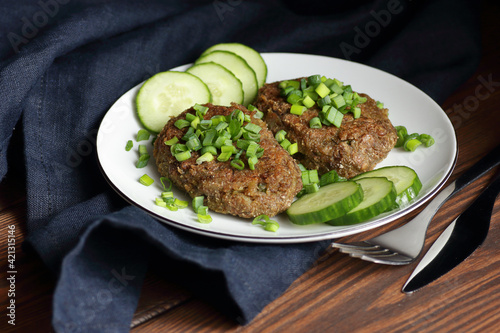 Lentil cutlets garnished with green onions and cucumber on rustic wooden table, closeup, vegetarian lenten eastern dish, healthy vegan food concept