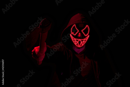 Man armed with an axe and wearing a scary lighting neon glow mask and a hoodie on black background. photo