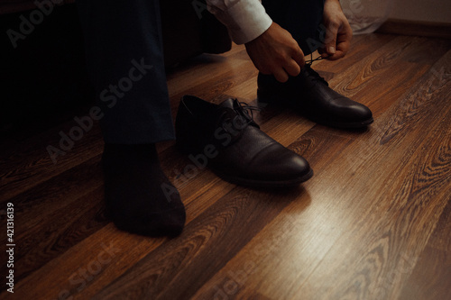 a strict man in a white shirt ties the laces on classic leather boots while sitting on the floor