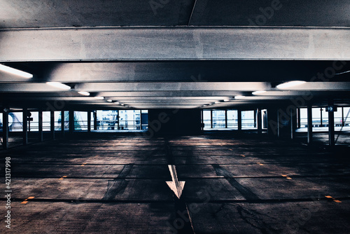 Cinematic and empty parking garage of shopping center with empty parking spaces, illuminated, concrete ceiling with steel girders, direction arrow on the floor, industrial architecture, Neu-Ulm