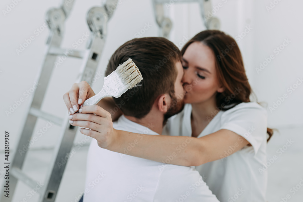 Happy lovers newlyweds a man and a woman are repair in renovation update improvement of the room kissing hugging relaxing preparing to move to a new house apartment, selective focus Happy lovers newlyweds a man and a woman are repair in renovation update improvement of the room kissing hugging relaxing preparing to move to a new house apartment, selective focus