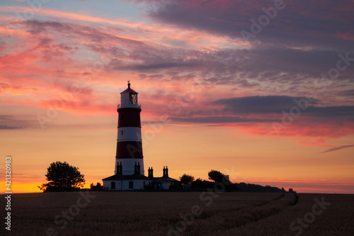 Happisburgh lighthouse on the East Coast of England surrounded by a field of wheat with a stunning sunset in the background