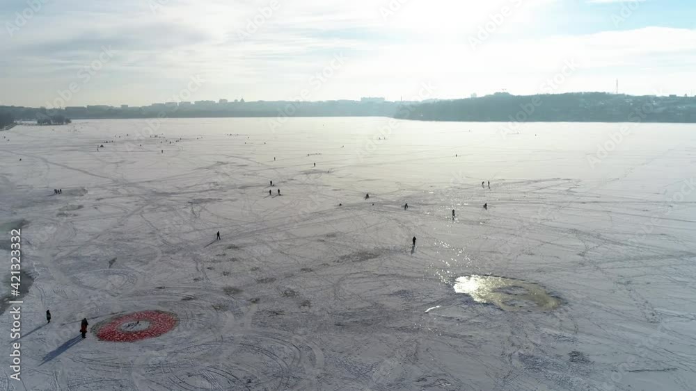 Flying out from the frozen lake with snow with people walking near the city