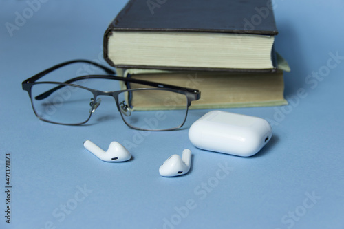 Workspace with glasses,wireless earphone and book on blue table, home office workspace concept.