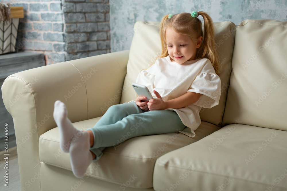 beautiful little girl on the couch with a mobile phone
