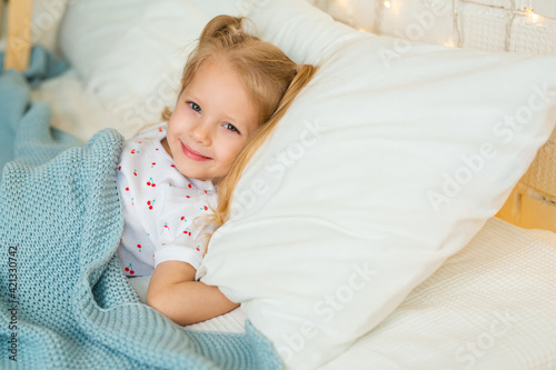 beautiful little girl lies in a bed on a pillow 