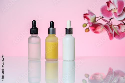 Three bottles of serum on a light pink background. Moisturizer, vitamin C, hyaluronic acid.
