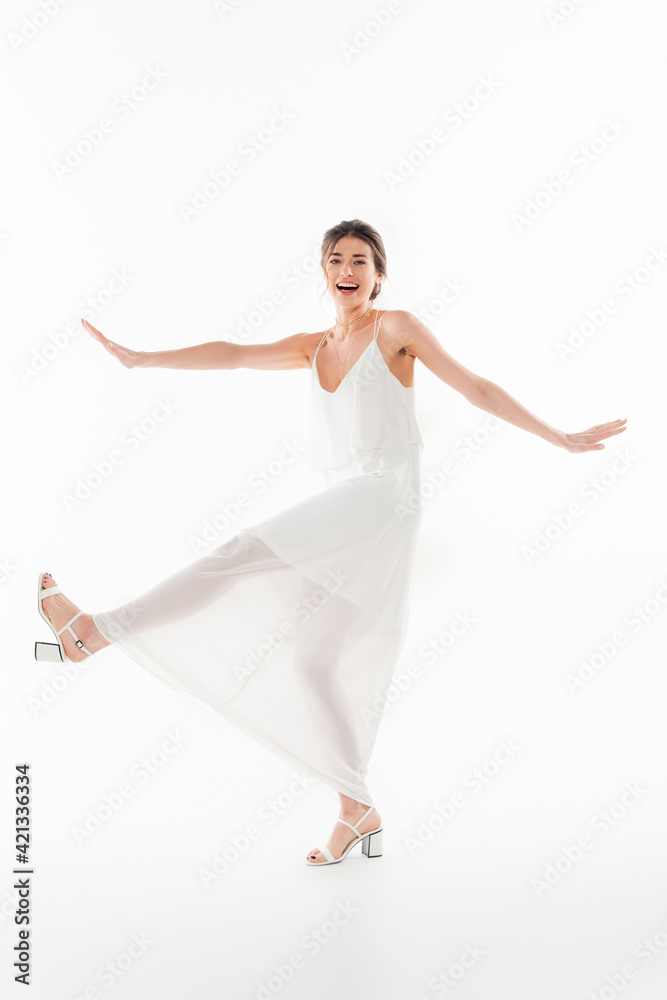 full length view of cheerful bride looking at camera while dancing on white
