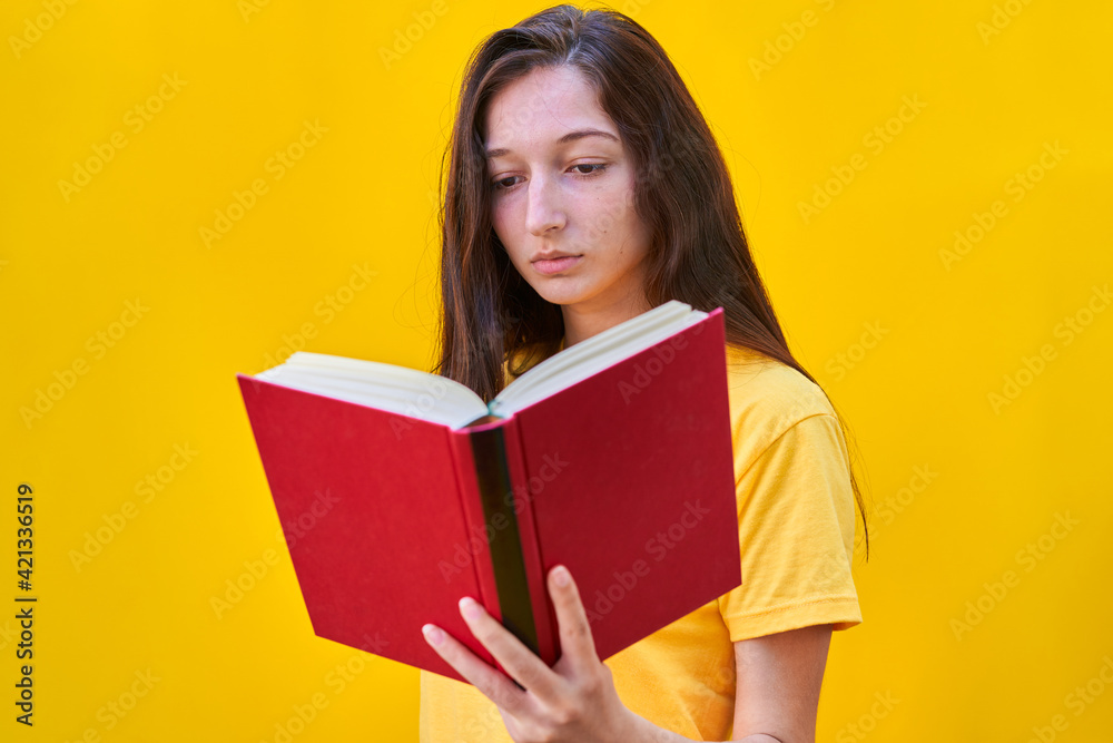 Caucasian young girl with reading a red book on yellow background Caucasian young girl with reading a red book on yellow background