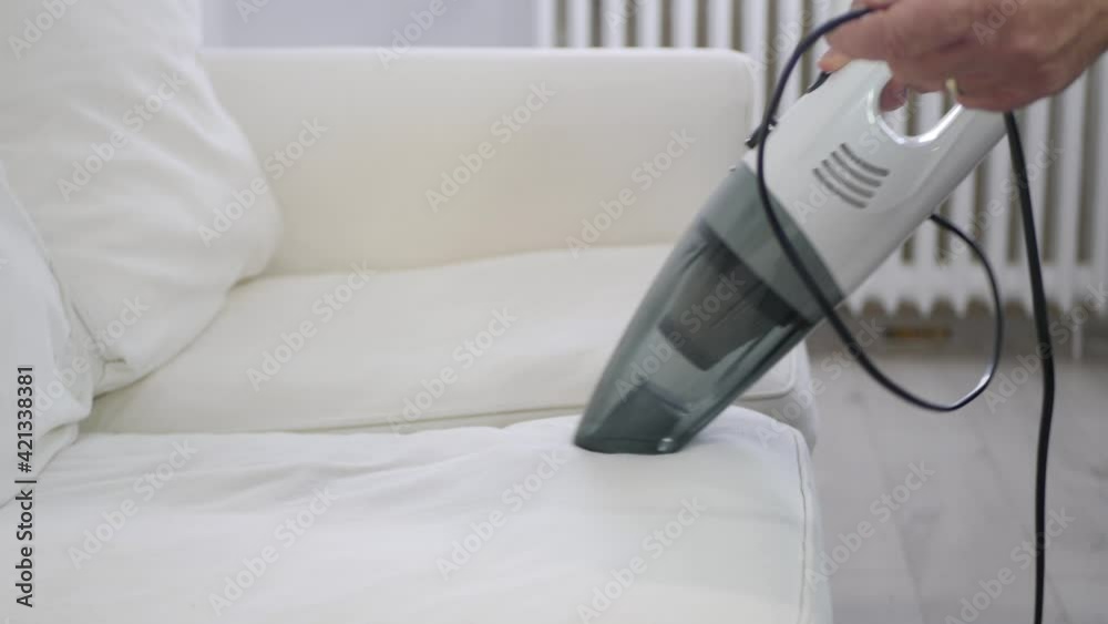 Man Using a Vacuum Cleaner in Household Activities to Clean the Sofa Surface from Dust. Man Using a Vacuum Cleaner in Household Activities to Clean the Sofa Surface from Dust.
