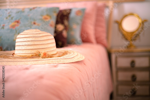 Stylish women sun hat lying on the bed next to the nightstand with a mirror. Elegance in a feminine style. Interior, Retro photo