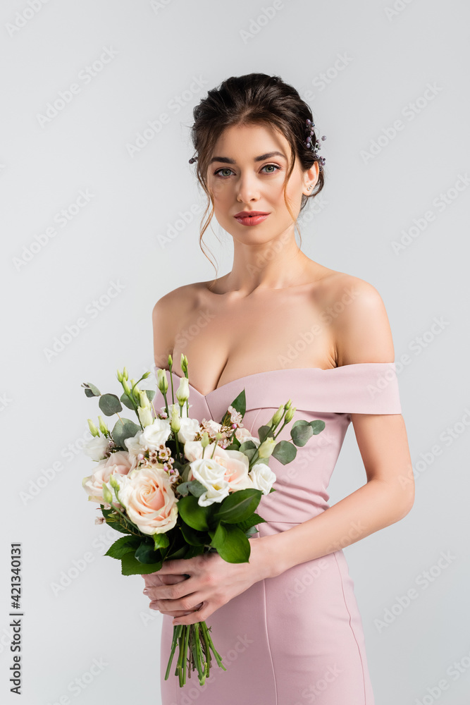 charming bride looking at camera while holding wedding bouquet isolated on grey charming bride looking at camera while holding wedding bouquet isolated on grey