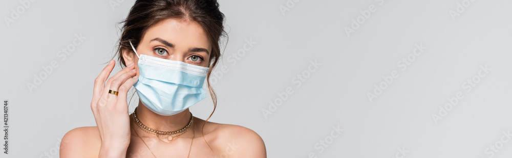 young bride in medical mask looking at camera isolated on grey, banner