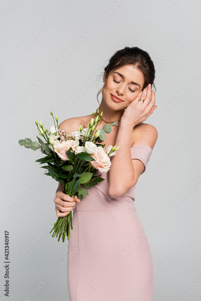happy bride in wedding ring posing with closed eyes and flowers isolated on grey
