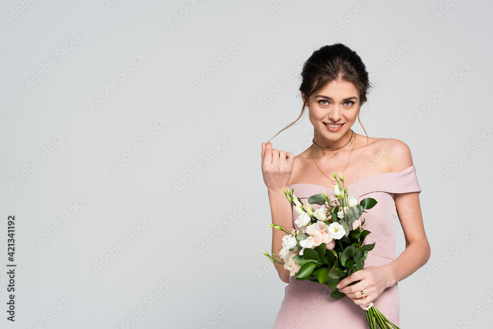 flirty woman touching hair and smiling at camera while holding wedding bouquet isolated on grey flirty woman touching hair and smiling at camera while holding wedding bouquet isolated on grey