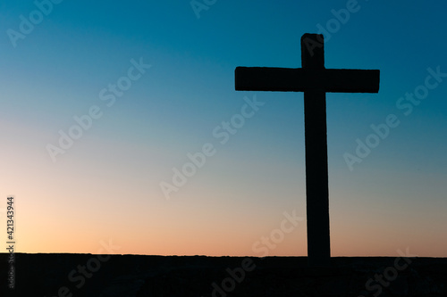 A silhouette of a stone cross ate the end of the day during the golden hour