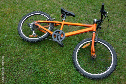 A teenage two-wheeled bicycle in orange color on the green grass.