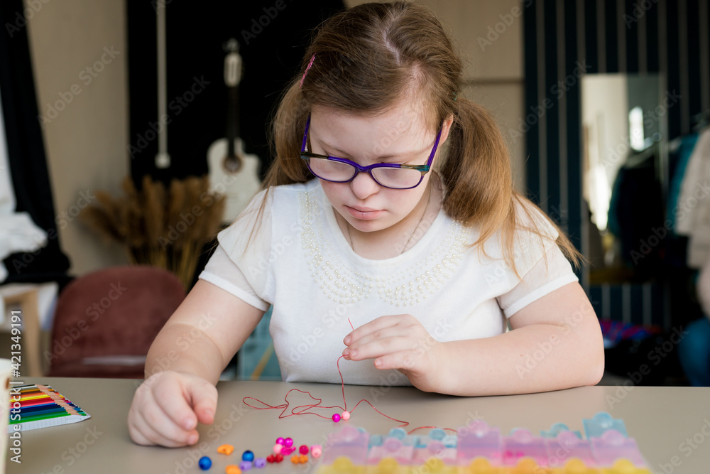 Cute teen girl stringing beads and making bracelet. Down syndrome kid crafting jewelry and threading beads. Play and development of capacity disability children Cute teen girl stringing beads and making bracelet. Down syndrome kid crafting jewelry and threading beads. Play and development of capacity disability children