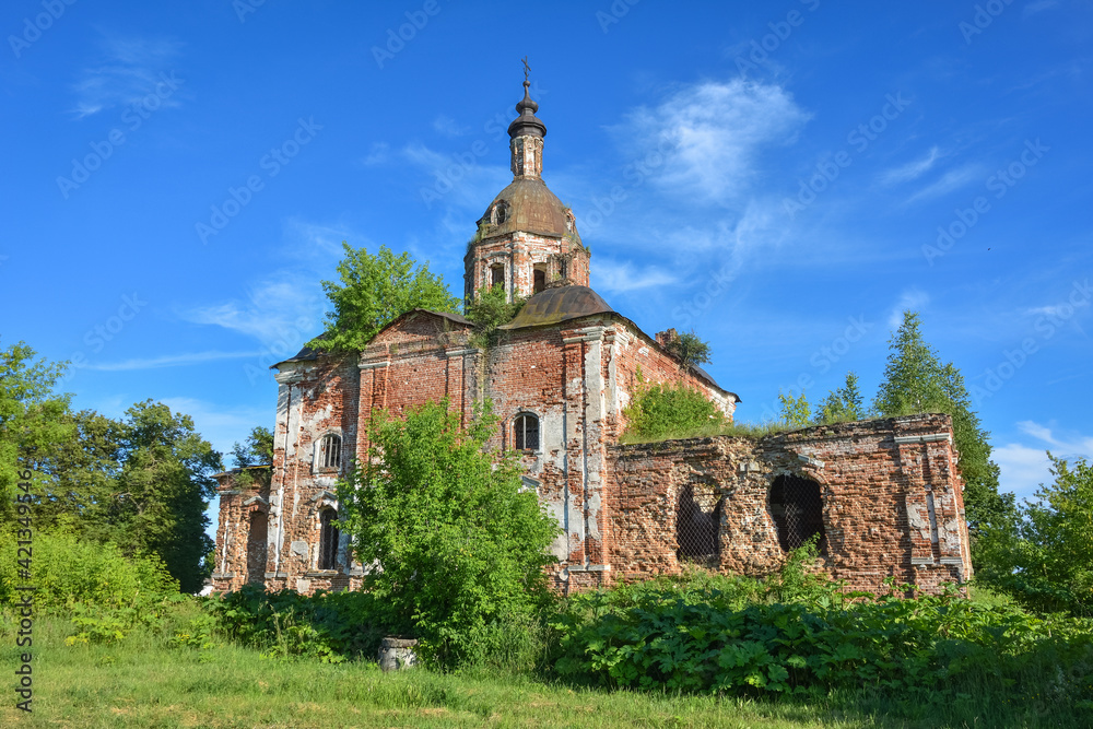 an abandoned dilapidated church, overgrown with grass against the background of the sky, surrounded by greenery