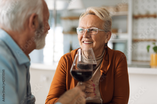 Happy mature woman talking to her husband while enjoying in wine at home