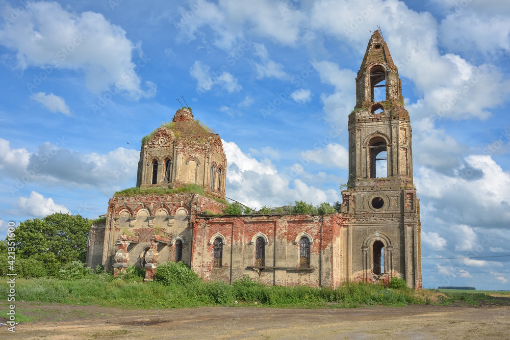 ruined church with a bell tower overgrown with grass against a cloudy sky, side view