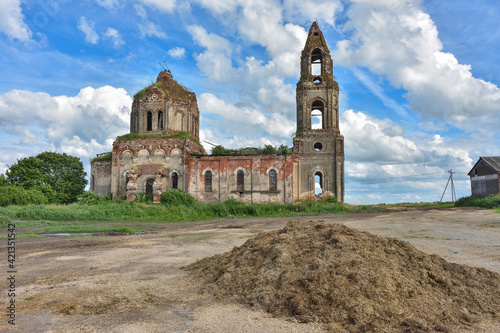 ruined church with a bell tower overgrown with grass against a cloudy sky, side view