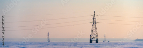 Industrial high voltage electricity tower in snow field at winter. Wide banner