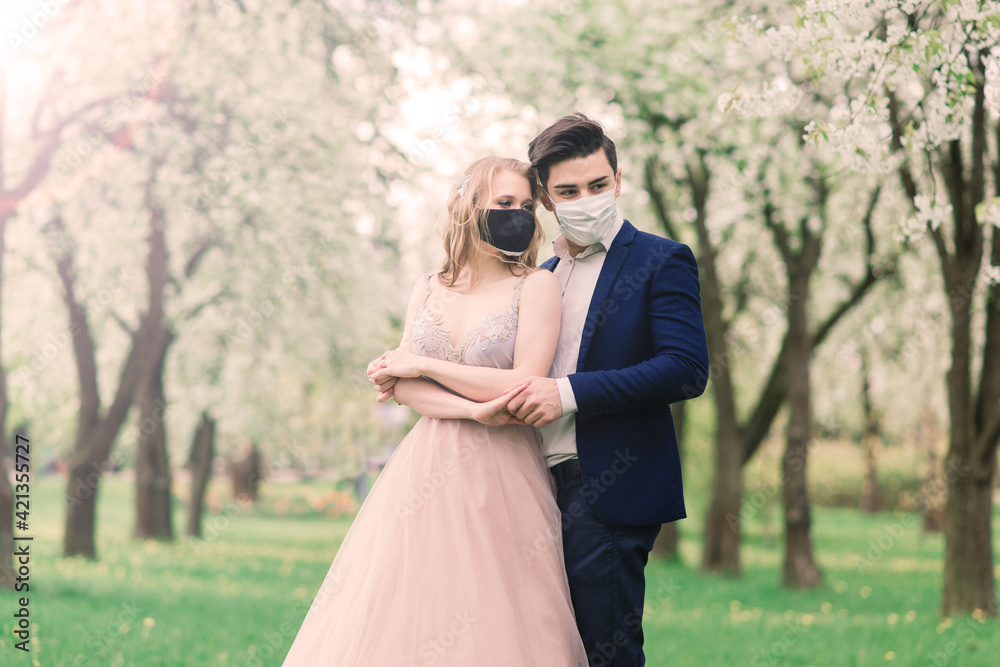 Young loving couple walking in medical masks in the park during quarantine on their wedding day. Young loving couple walking in medical masks in the park during quarantine on their wedding day.