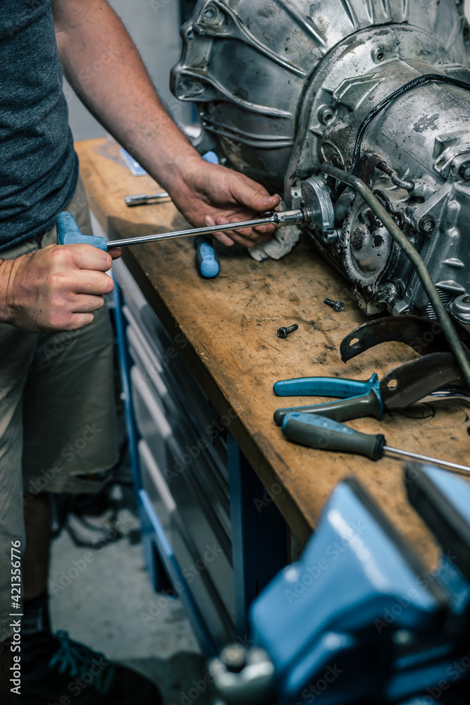 Fototapeta premium Young caucasian male is seen wrenching an automatic gearbox of an old vintage car. Tune up or checkup of a vintage car.