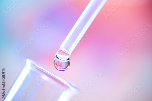 Close up of chemical test tube and pipette with drop of colorless liquid on purple background