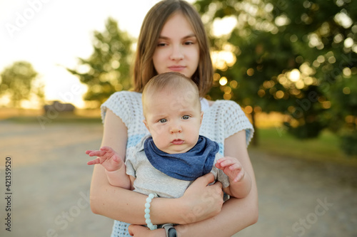 Cute big sister admiring her baby brother. Adorable teenage girl holding her new baby boy brother. Kids with large age gap. Big age difference between siblings.