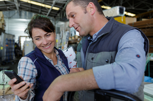 happy warehouse workers showing smartphone to colleague