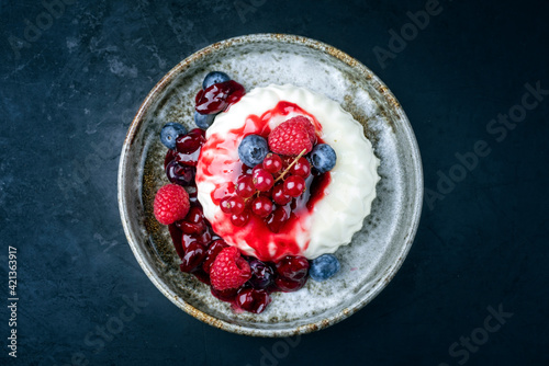 Modern style traditional blancmange almond pudding with wild berry coulis served as top view in a Nordic design plate on black background with copy space photo