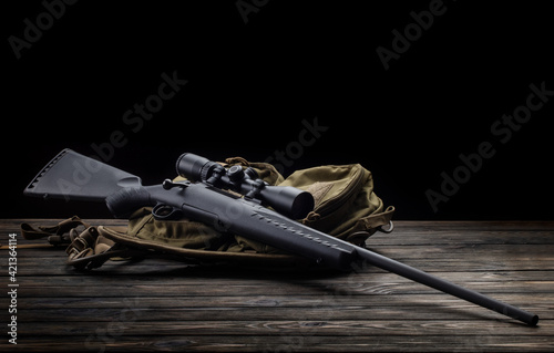 Modern bolt rifle with a telescopic sight on a dark back. Sniper weapon on a wooden table.