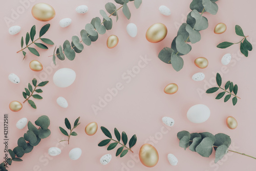 Easter flat lay composition. Luxury white and gold Easter eggs decorated green and eucalyptus leaves on pink table. Flat lay, top view copyspace frame