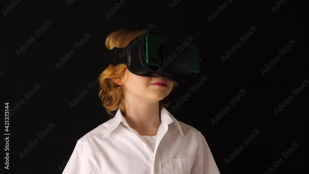 Blonde boy looks with virtual reality glasses and watching VR 360 video against black background Blonde boy looks with virtual reality glasses and watching VR 360 video against black background