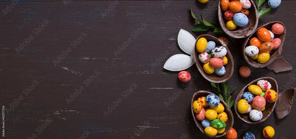 Banner with chocolate eggs and bunny on wooden table copy space. Happy Easter eggs hunt concept background. View from above