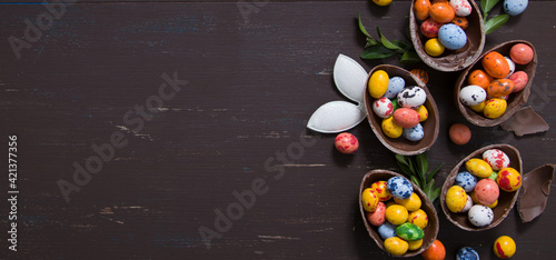 Banner with chocolate eggs and bunny on wooden table copy space. Happy Easter eggs hunt concept background. View from above