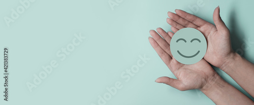 Hand holding green paper cut happy smile face on green background , positive thinking, mental health assessment , world mental health day concept 
