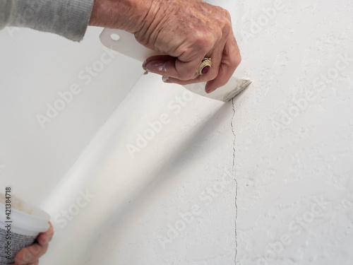 Man repairing interior wall crack damage. Concrete masonry wall patch with spatula and plaster.