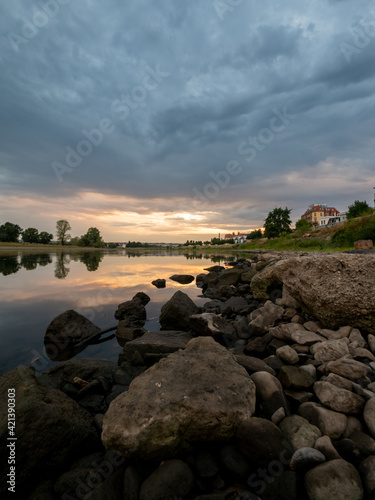 Beautiful sunset at Dresden Elbe River banks with reflections in the water of the dramatic cloudy sky. Evening sunlight at the clouds and an idyllic landscape in the nature.