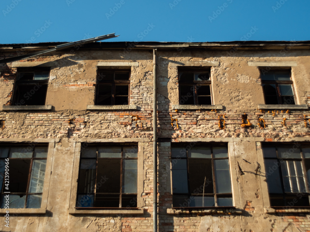 Facade of an abandoned old ruin with broken windows and a brick wall with weathered stones Facade of an abandoned old ruin with broken windows and a brick wall with weathered stones