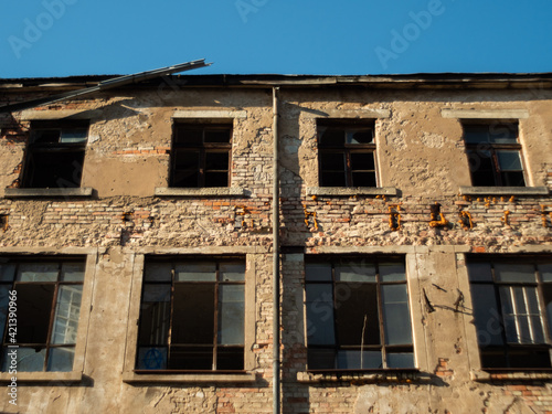 Facade of an abandoned old ruin with broken windows and a brick wall with weathered stones