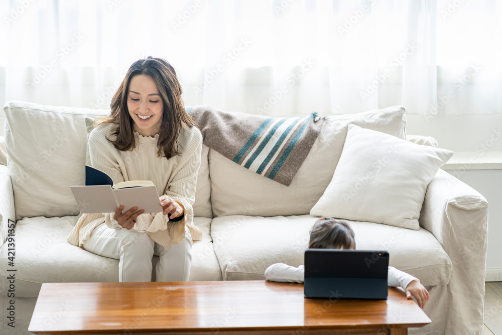 タブレットPCを見る日本人の女の子と読書をする母親 タブレットPCを見る日本人の女の子と読書をする母親