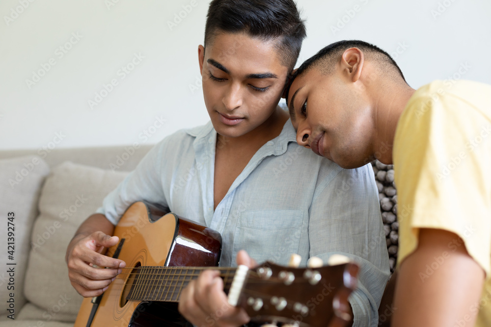 Diverse gay male couple sitting on sofa playing guitar Stock Photo | Adobe  Stock