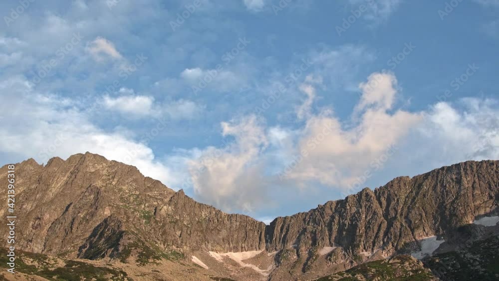 Cumulus clouds float over rocky ridge in blue sky. View of mountain system with glacier on slope. Preparation for ascent, conquest of summit Cumulus clouds float over rocky ridge in blue sky. View of mountain system with glacier on slope. Preparation for ascent, conquest of summit