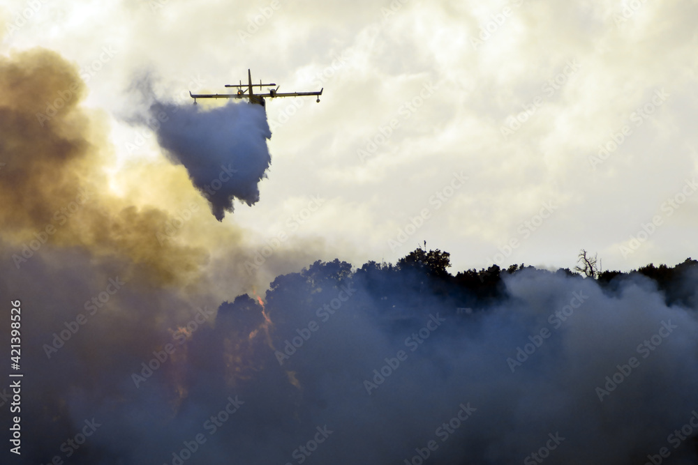big fire in the mountains with high flames and a long tongue of fire between big clouds of smoke and a firefighting plane dumps water on the fire to try to tame it big fire in the mountains with high flames and a long tongue of fire between big clouds of smoke and a firefighting plane dumps water on the fire to try to tame it