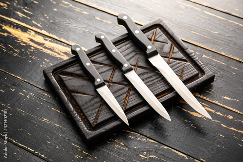 Board with set of knives on dark wooden background