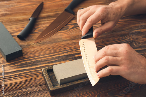 Man sharpening knife on wooden background photo