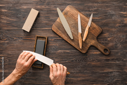 Leinwand Poster Man sharpening knife on wooden background